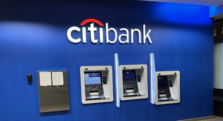 Spotlights on a Citibank logo against a blue background, placed above three ATM wall kiosks.