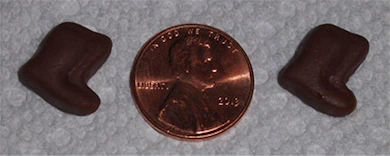 Two small chocolate-shaped socks, one on each side of a 2013 U.S. penny, placed on a light textured surface for size comparison.